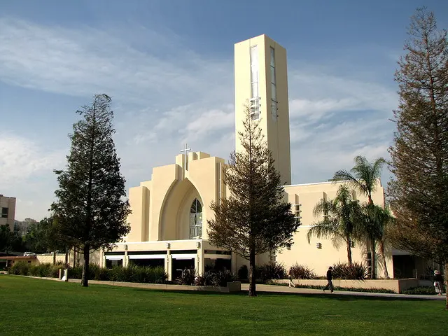 Modern cream-coloured Loma Linda University Church of Seventh-day Adventists with a tall bell tower and palm trees on the lawn.