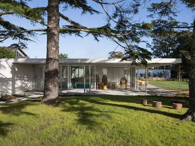 A single-storey preschool building with large glass doors opening onto a lawn, child-sized furniture visible inside