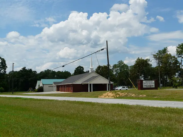Brick Christian church with a white steeple and green metal roof, beside a roadside sign reading Christian Faith Church