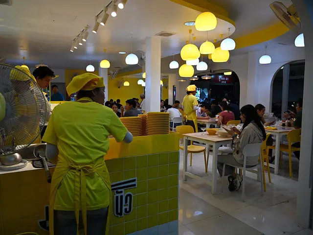 Staff in yellow uniforms serving diners at tables inside a brightly lit restaurant.