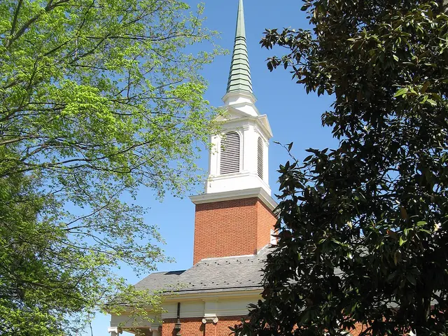 Brick bell tower and green copper spire of First Presbyterian Church in Charlottesville, Virginia, framed by spring tree foliage.