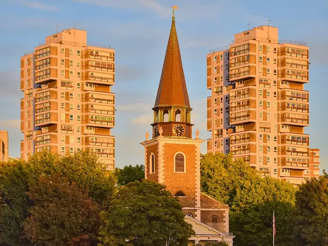 The exterior of a stone church tower and building flanked by residential houses at dusk.