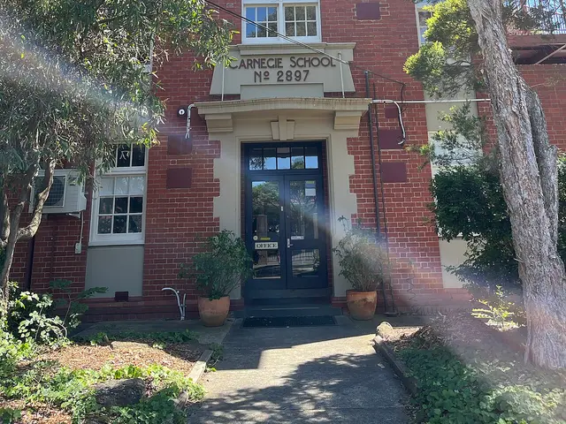 The brick entrance of Carnegie School, a heritage primary school building framed by trees.