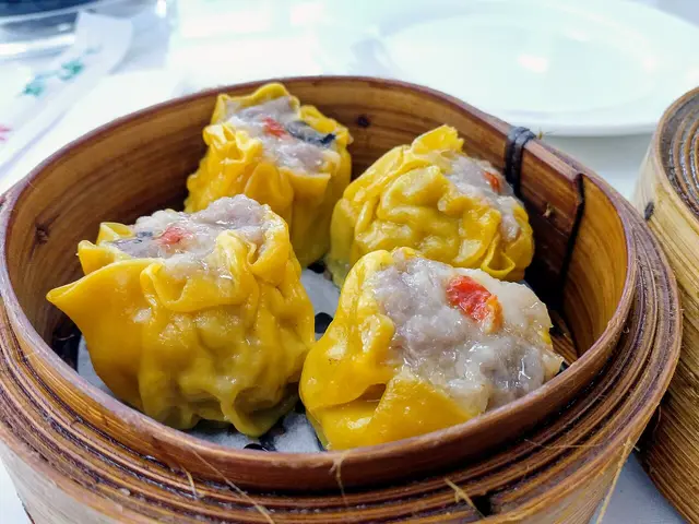 Dim sum dumplings with yellow wrapping and a red berry topping in a steamer basket.
