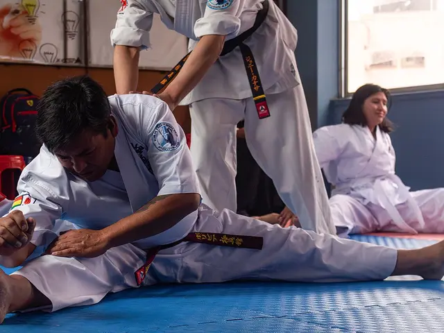 Karate students in white gis practising a stretching exercise on blue mats at Musha Dojo.