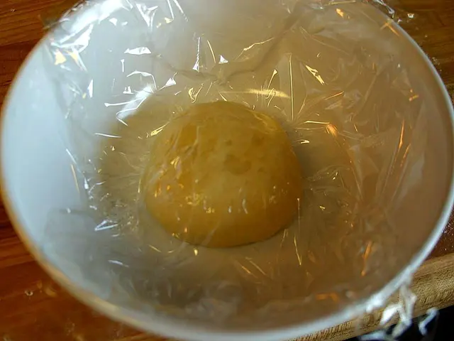 Hands kneading pizza dough on a kitchen counter.