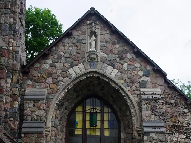 The front exterior of a stone church building with a tall steeple.