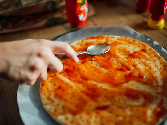 Hands spreading tomato sauce over homemade pizza dough.
