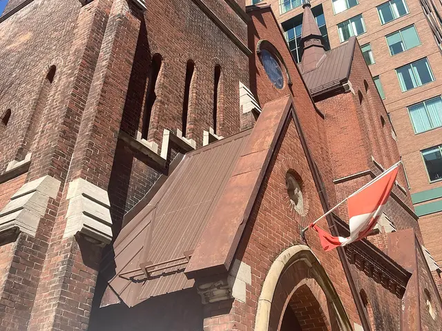 Upward view of the brick bell tower of St. Peter and St. Paul Anglican Church in Ottawa, Ontario, with a Canadian flag and street sign in the foreground.