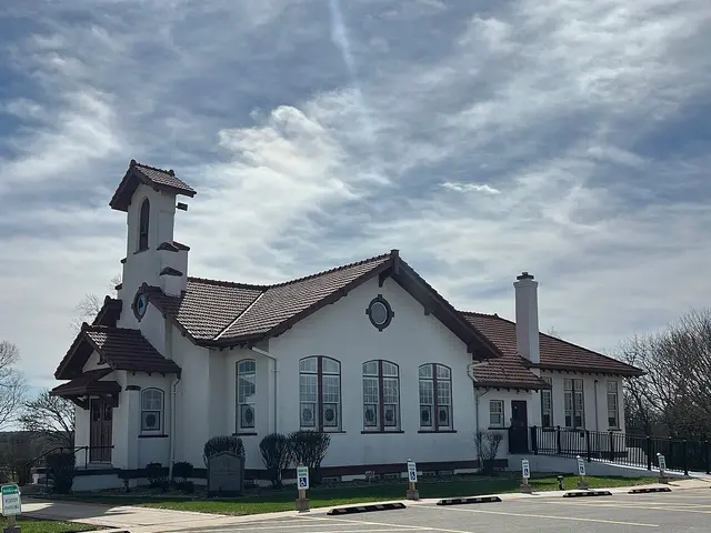 White stucco Christian church with a bell tower topped by a spire, parking area in front