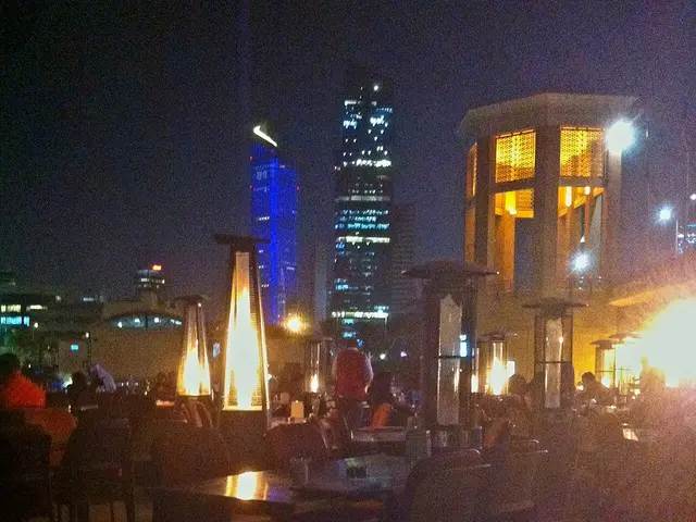 Outdoor restaurant seating area at night with patio heaters and string lighting.