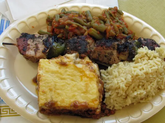 A plate of Greek foods including moussaka, string beans and pork souvlaki with rice pilaf.