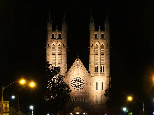 Twin-towered Gothic Revival Catholic basilica illuminated at night, with a large rose window between the spires