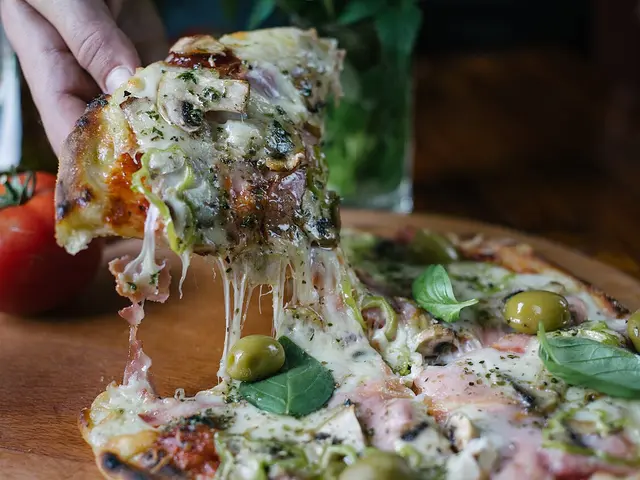 A hand pulling a slice of pizza away from the rest of the pie, with melted cheese stretching between them.