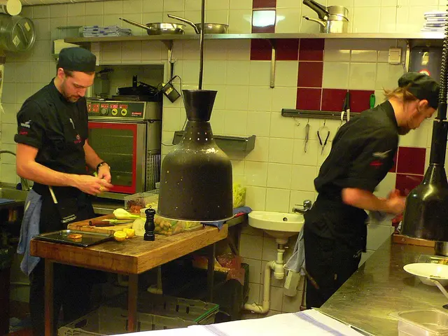 Chefs preparing food in the open kitchen of a restaurant.