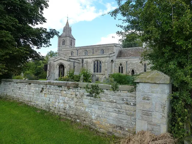 The exterior of a small stone village church surrounded by trees.