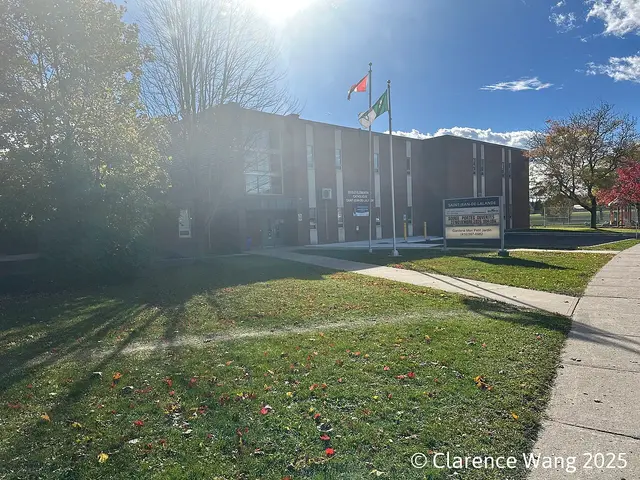 The exterior of a Catholic elementary school building with flagpoles out front and a sign bearing the school's name.