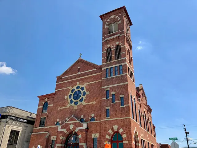 First Presbyterian Church in Greensburg, Indiana, a Romanesque-style red brick church with a tall square corner tower, viewed from below against a blue sky.