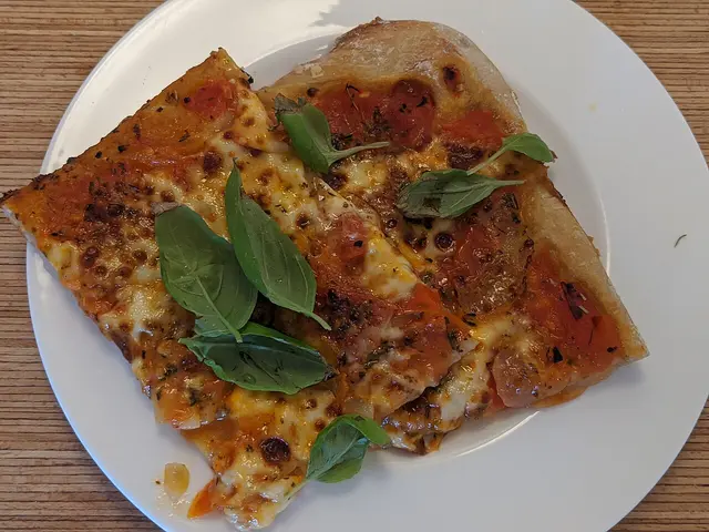 A margherita pizza with melted mozzarella and basil leaves on a plate.