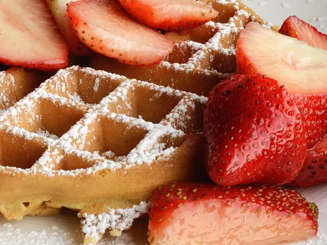 A waffle topped with strawberries and confectioner's sugar.