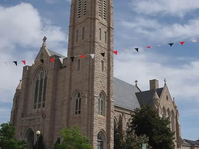 Tall sandstone Gothic Revival Catholic cathedral with a square bell tower, decorated with pennant bunting