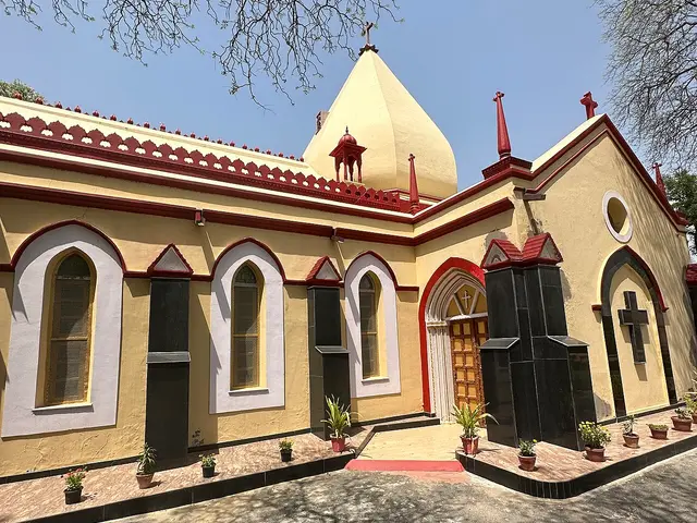Exterior of Sacred Heart Catholic Church, a yellow stucco building with a domed spire and red trim.
