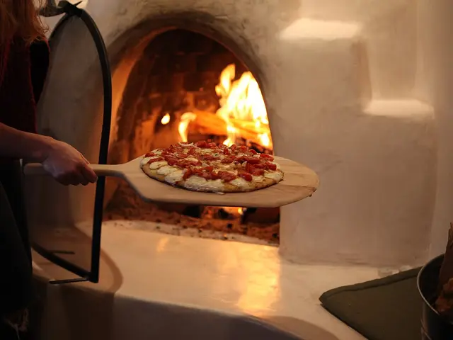 A pizza baking on the stone floor of a wood-fired oven.