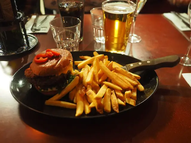 A burger served on a plate next to a glass of beer at a restaurant table.