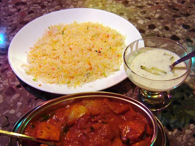 A plate of chicken tikka jalfrezi served with pilau rice and cucumber raita at an Indian restaurant.