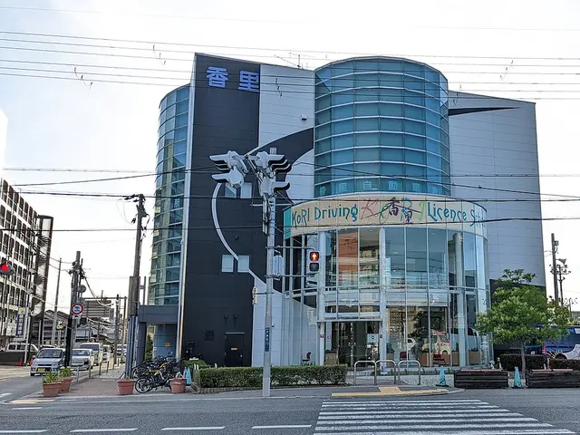 The glass-fronted, curved exterior of Kori Driving Licence School in Japan, with a branded van parked outside.