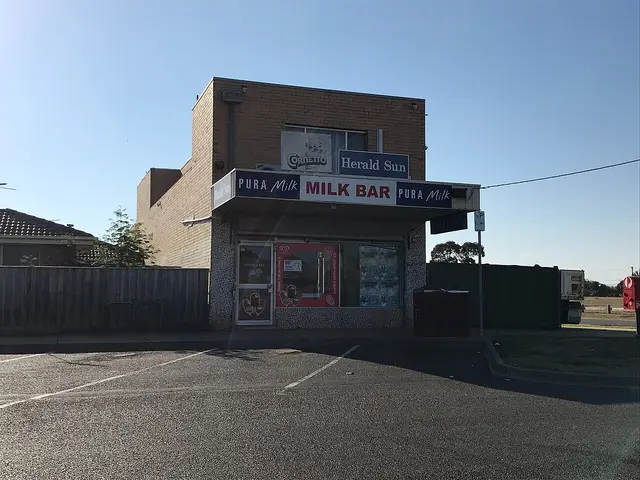A small brick milk bar corner store with hand-painted signage on a suburban street