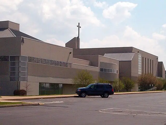 Large contemporary Christian church building with a slim cross-topped spire, seen across an empty parking lot