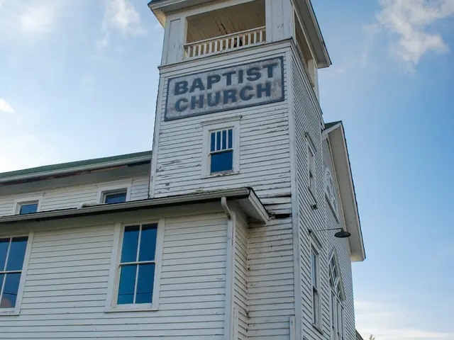 Weathered white wooden Baptist church with a corner bell tower painted with 'Baptist Church' signage.