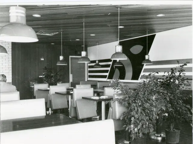 Interior of a restaurant dining room with booths and tables arranged under overhead light fixtures.
