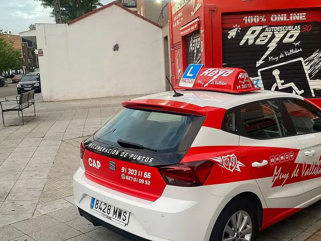 A red and white branded car parked outside the Autoescuelas Rayo driving school storefront in Spain.