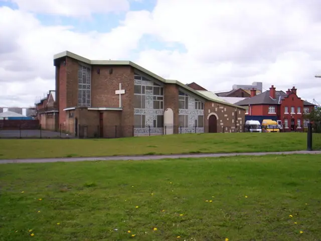 Exterior of St. Joan of Arc Roman Catholic Church in Bootle, a modern brick church building with a tall white cross on its gable.