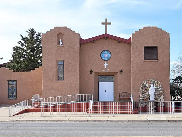 Adobe-style Catholic church with a stepped parapet, round stained-glass window, and statue niche beside the entrance