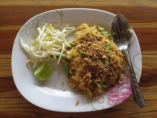 A plate of pad Thai with bean sprouts and lime.