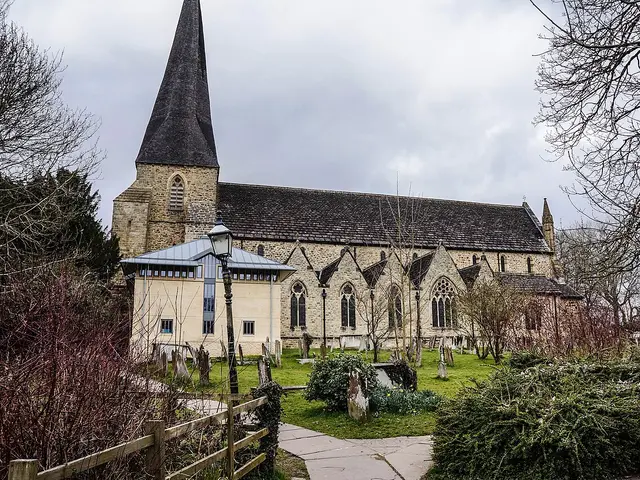 Exterior of St Mary's parish church in Horsham, West Sussex, a stone Anglican church with a shingled spire, seen from a graveyard.