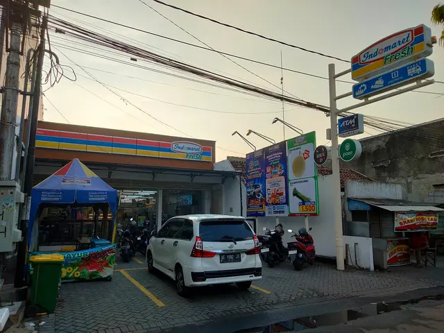 The exterior of an Indomaret Fresh minimarket at dusk in Indonesia, with a car parked in front