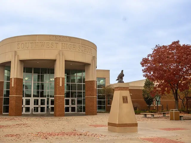 The curved stone entrance of Lincoln Southwest High School with a bronze falcon statue in the courtyard.