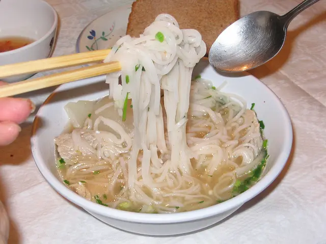 A bowl of Vietnamese pho noodle soup with herbs and lime.