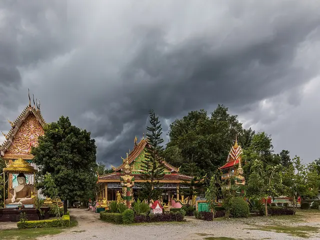 Buddhist temple complex with multiple ornate, multi-tiered roofed pavilions under a dramatic stormy sky in Vang Vieng, Laos.