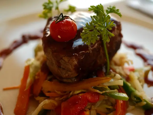 A plated serving of meat with a cherry tomato and sauteed vegetables at a restaurant.