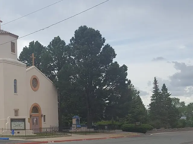 Cream stucco Catholic church with an octagonal bell tower and tiled roof, cars parked outside
