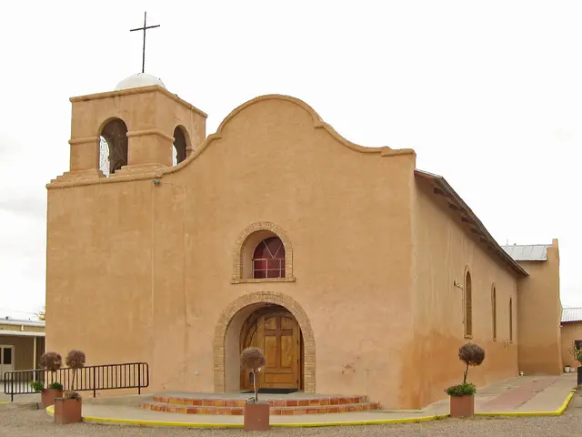 Tan adobe Catholic church with a domed bell tower topped by a cross, seen from the side