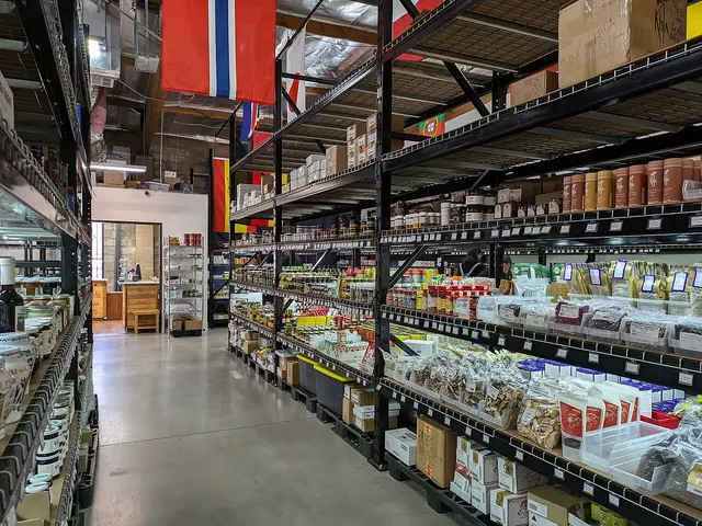 Interior aisle of a gourmet food store lined with shelves of specialty jars, tins, and packaged goods beneath international flags.