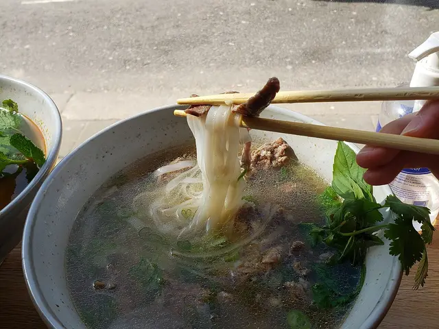 A bowl of Vietnamese pho with steak on a window-side table.