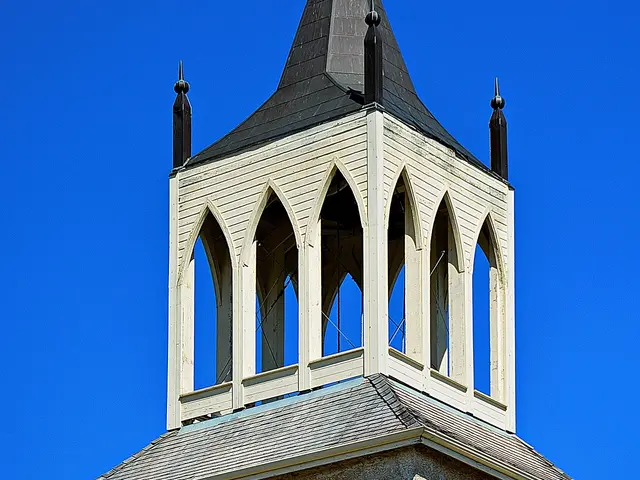 Close-up of the stone bell tower and open lantern spire of St. Andrew's Anglican Church against a clear blue sky.