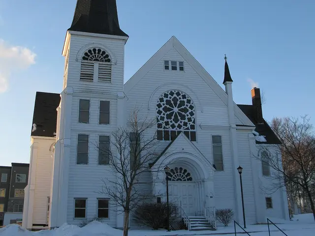 Tall white wooden United Church with a steep steeple and a round rose window, photographed in winter in Sackville, New Brunswick.